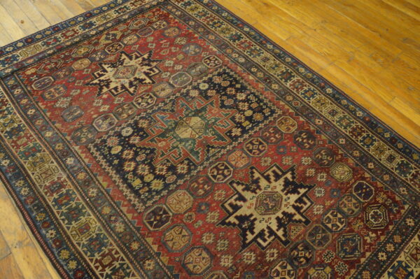 Distressed red and blue tribal rug featuring complex geometric medallions rests on light wood plank flooring.