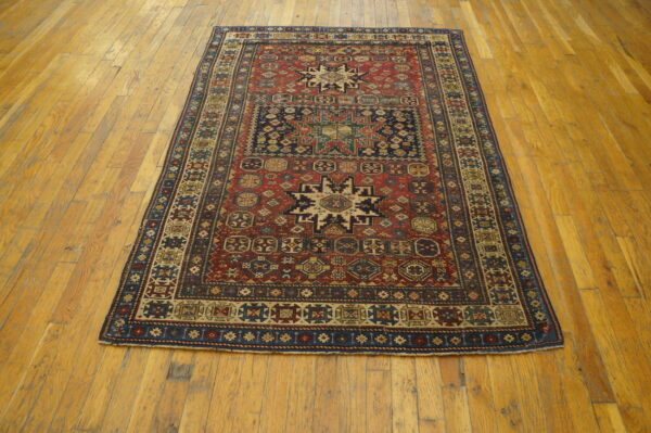 Red and navy tribal pattern rug with geometric designs displayed on light brown wood plank flooring.