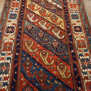 Diagonal striped runner rug in red, navy, teal, and cream with detailed geometric motifs on wood flooring.