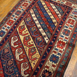 Red, blue, and cream runner with intricate diagonal stripes and boteh designs on worn wooden flooring.