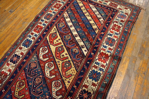 Red, blue, and cream runner with intricate diagonal stripes and boteh designs on worn wooden flooring.