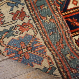 Blue, red, and cream geometric rug showing both pile and flatweave texture over gray wood flooring.