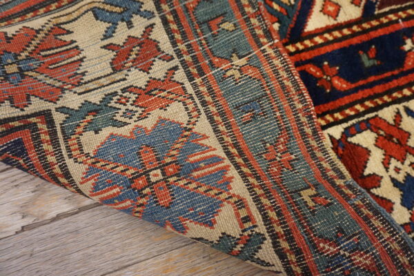 Blue, red, and cream geometric rug showing both pile and flatweave texture over gray wood flooring.
