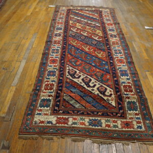 Red, blue, and cream runner rug with tribal diagonal stripes rests on worn wood flooring.