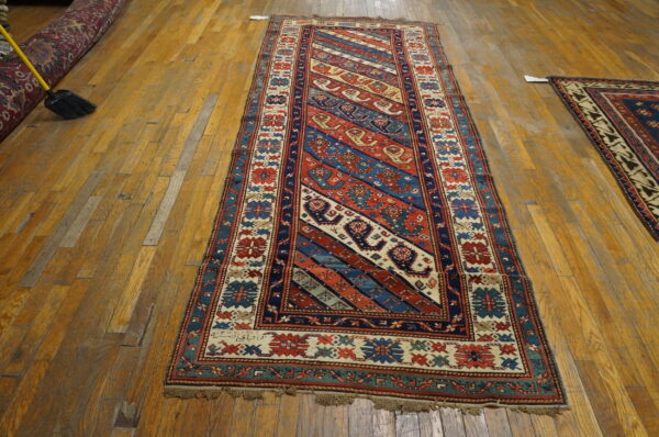 Red, blue, and cream runner rug with tribal diagonal stripes rests on worn wood flooring.