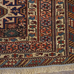 Low-pile rug corner showing detailed red and blue geometric patterns and knotted fringe on wood flooring.