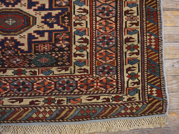 Low-pile rug corner showing detailed red and blue geometric patterns and knotted fringe on wood flooring.
