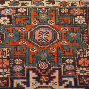 Geometric rug detail showing stepped medallions and floral motifs in rich teal, rust, and blue.