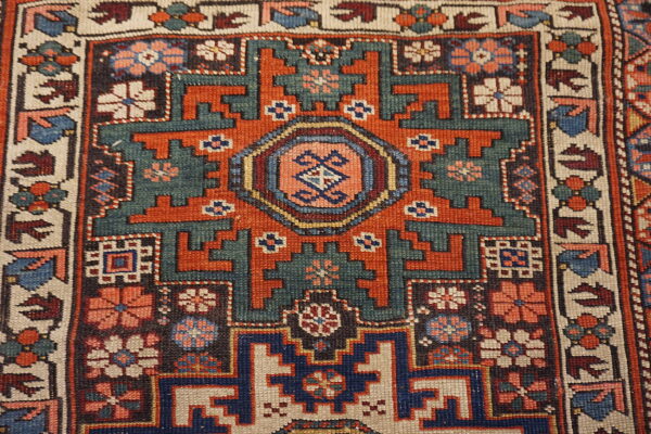 Geometric rug detail showing stepped medallions and floral motifs in rich teal, rust, and blue.