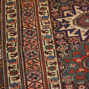 Low-pile rug with complex geometric patterns in red, navy, teal, and beige on wood planks.