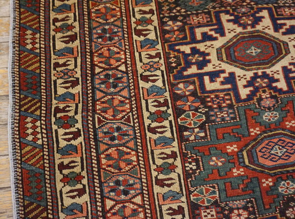 Low-pile rug with complex geometric patterns in red, navy, teal, and beige on wood planks.
