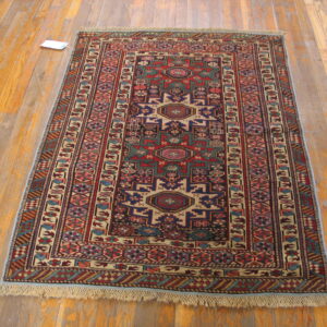 Rectangular low-pile rug featuring complex red and blue tribal geometric patterns displayed on wood flooring.