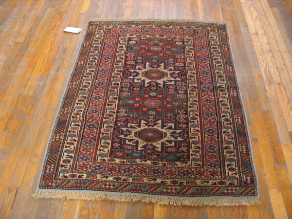 Rectangular low-pile rug featuring complex red and blue tribal geometric patterns displayed on wood flooring.