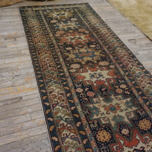 Long geometric runner rug featuring navy, rust, and tan designs on distressed gray wood floors.