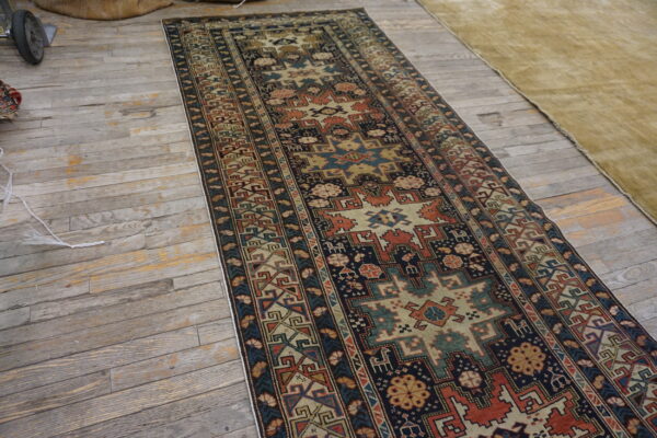 Long geometric runner rug featuring navy, rust, and tan designs on distressed gray wood floors.