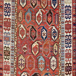 A high-pile, traditional red rug featuring rows of multicolored geometric elongated medallion patterns and wide borders.