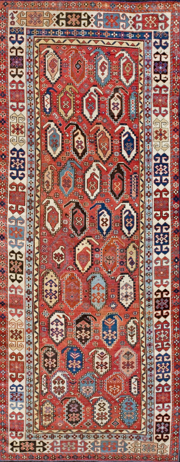 A high-pile, traditional red rug featuring rows of multicolored geometric elongated medallion patterns and wide borders.