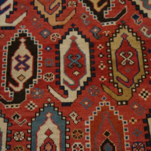 Close-up of a rug with a red field featuring stepped medallions in blue, cream, black, and tan.
