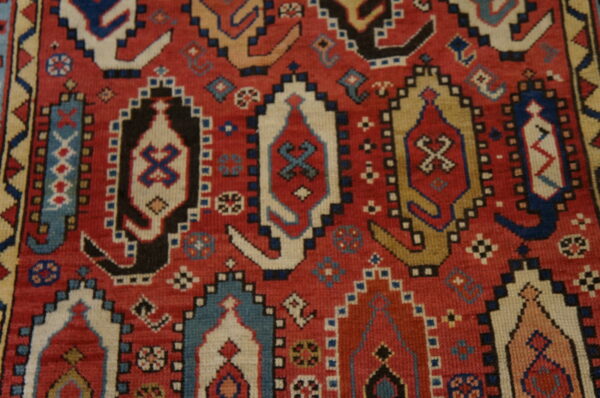 Close-up of a rug with a red field featuring stepped medallions in blue, cream, black, and tan.