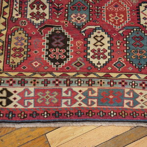 Red, blue, and tan geometric tribal rug with low pile rests on light wood plank flooring.