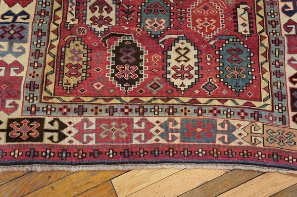 Red, blue, and tan geometric tribal rug with low pile rests on light wood plank flooring.
