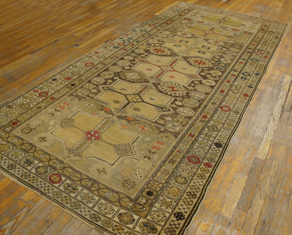 Elongated beige and brown tribal rug with geometric medallions lying on worn wooden planks.