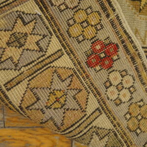 Low-pile rug with beige, tan, and red geometric patterns rolled up over distressed wood planks.