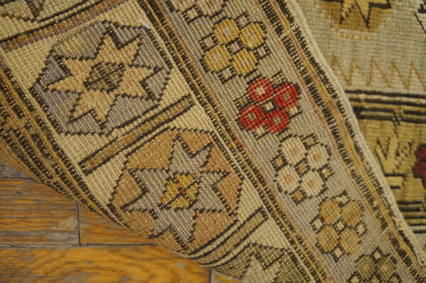Low-pile rug with beige, tan, and red geometric patterns rolled up over distressed wood planks.