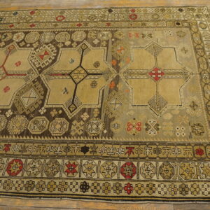 Muted geometric rug with khaki, brown, and red accents displaying large star patterns on wood flooring.