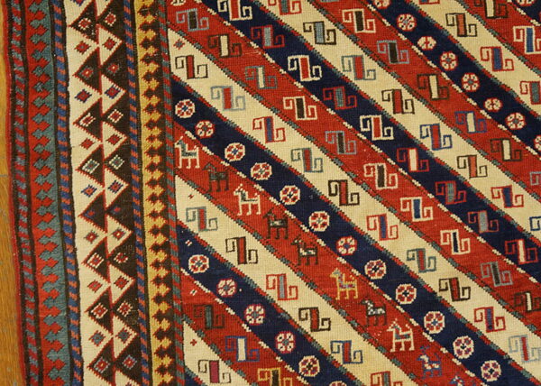 Red, navy, and cream rug detail showing diagonal stripes, geometric hooked symbols, and small stylized horses.