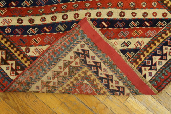 Red, navy, and cream geometric rug with a corner folded over, revealing the detailed flatweave reverse on wood.