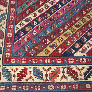 Low-pile rug corner showing diagonal red, blue, and yellow stripes meeting a cream geometric border.