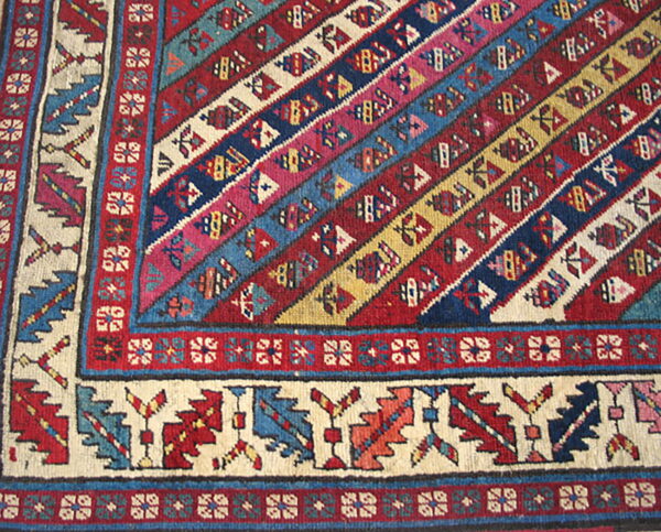 Low-pile rug corner showing diagonal red, blue, and yellow stripes meeting a cream geometric border.