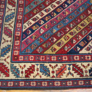 Geometric rug corner featuring colorful diagonal bands of red, blue, and cream resting on hardwood flooring.