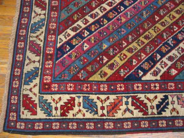 Geometric rug corner featuring colorful diagonal bands of red, blue, and cream resting on hardwood flooring.