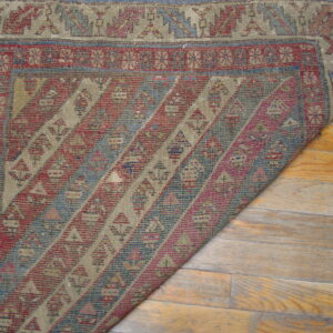 Geometric flatweave rug in muted red, blue, and beige is partially folded over glossy wood floors.