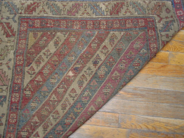 Geometric flatweave rug in muted red, blue, and beige is partially folded over glossy wood floors.