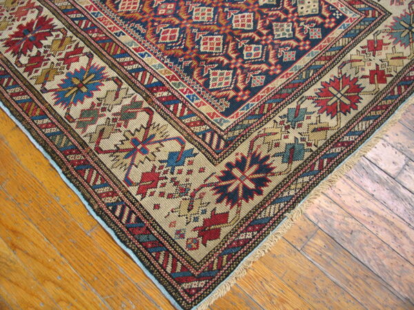 A detailed corner of a dense, patterned rug displaying red, navy, and tan colors on worn wooden planks.