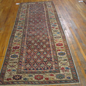 Navy and red geometric runner rug with a wide cream border sits on worn wooden flooring.