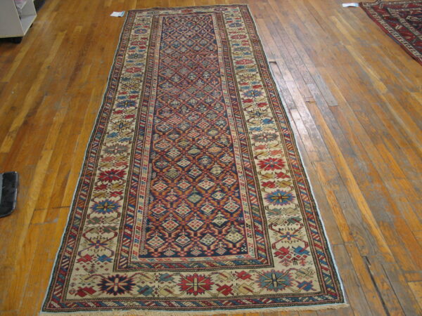 Navy and red geometric runner rug with a wide cream border sits on worn wooden flooring.