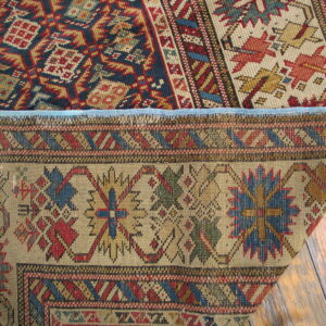 Geometric rug in red, blue, and tan folded to reveal its flat woven backing on distressed wood floors.