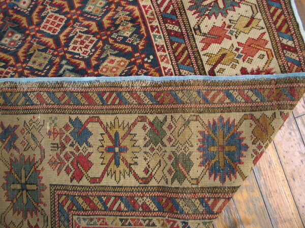 Geometric rug in red, blue, and tan folded to reveal its flat woven backing on distressed wood floors.