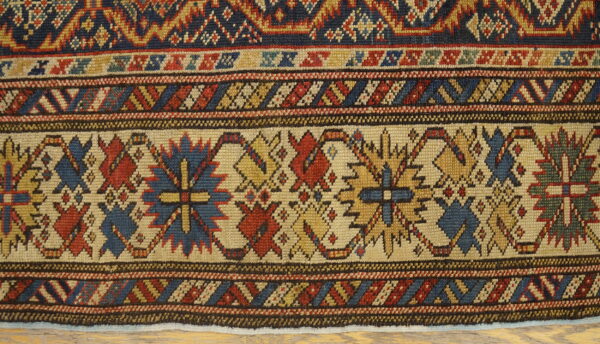 Multi-band geometric rug pattern in rich navy, red, and gold, shown closely over light wood floor.