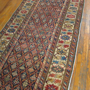 Geometric runner rug with navy blue field, red diamonds, and colorful borders on worn wood floor planks.
