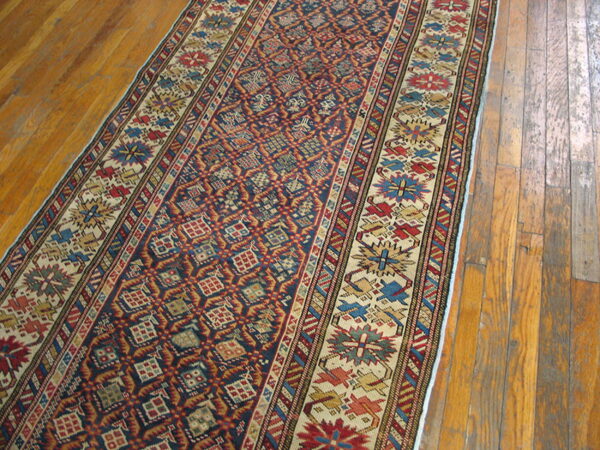 Geometric runner rug with navy blue field, red diamonds, and colorful borders on worn wood floor planks.