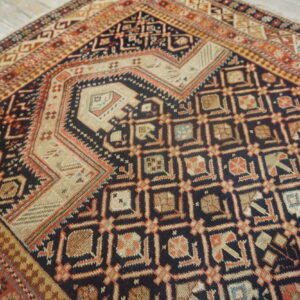 Geometric rug with complex dark blue, tan, and terracotta patterns displayed on light gray wood flooring.