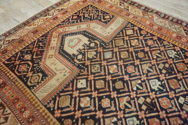 Geometric rug with complex dark blue, tan, and terracotta patterns displayed on light gray wood flooring.
