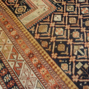 The navy and rust geometric rug with multiple borders rests partially on distressed gray wood flooring.