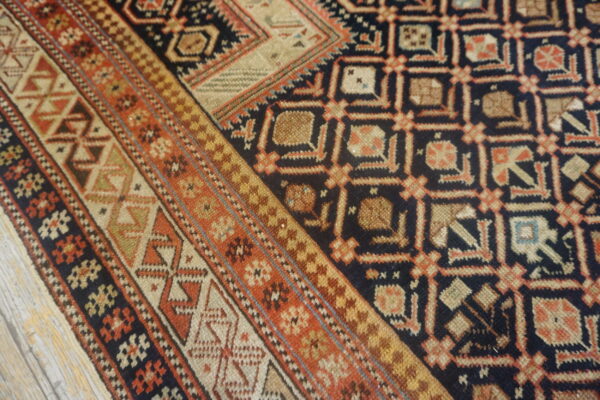 The navy and rust geometric rug with multiple borders rests partially on distressed gray wood flooring.