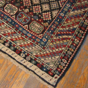 Intricate geometric rug corner featuring red, blue, black, and cream motifs on distressed wood planks.